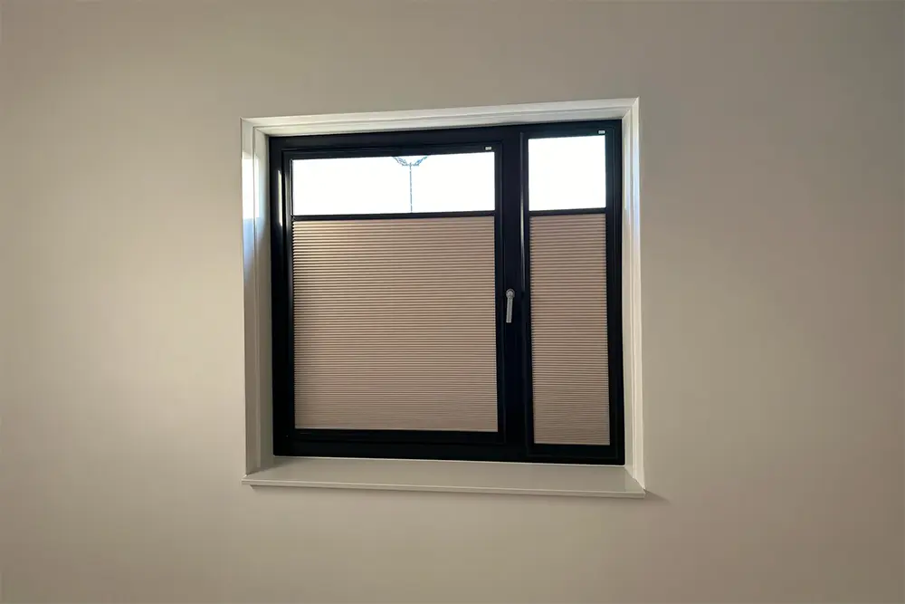 Verduisterend plisségordijn in beige op een raam met donker kozijn